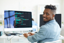 student sitting at a computer smiling towards the camera